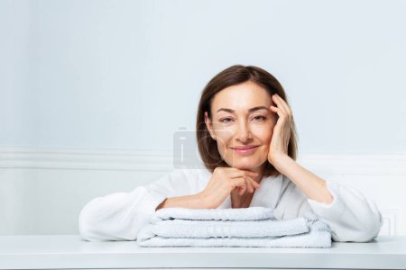 Téléchargez les photos : Portrait de beauté d'une femme dans son prime, avec un sourire confiant en housecoat posant dans l'installation de salle de bains mettant la main sur la serviette - en image libre de droit