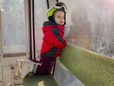 Téléchargez les photos : Petite skieuse assise dans le téléphérique prête à glisser sur les pistes des Alpes françaises à l'école de ski par temps ensoleillé - en image libre de droit