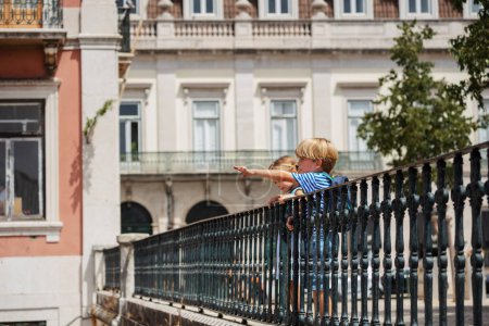 Foto de Jóvenes viajeros, niño y niña en el mirador de Lisboa señalando con los dedos, Portugal arquitectura en el fondo - Imagen libre de derechos