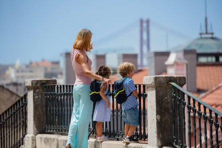 Photo for Mother with kids on vacations in Portugal standing looking at famous Lisbon bridge from city viewpoint in summer day - Royalty Free Image