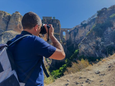 Foto de Turista masculino toma fotos del famoso Puente Nuevo en Ronda parado en el fondo del desfiladero de El Tajo durante su recorrido turístico por España - Imagen libre de derechos