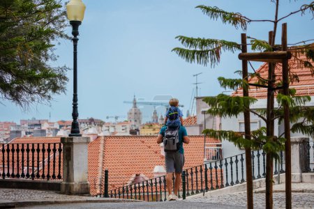 Téléchargez les photos : Portrait pleine hauteur d'un enfant assis sur les épaules du père, ils marchent dans des rues pavées et profitent d'un voyage d'été à Lisbonne - en image libre de droit