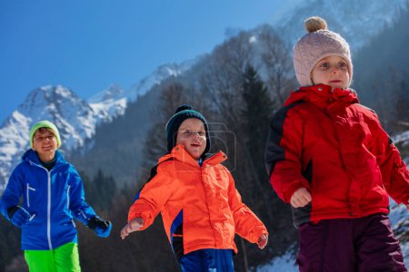 Téléchargez les photos : Heureux frères et sœurs courir dans la forêt de montagne profiter des vacances en station d'hiver par une journée ensoleillée - en image libre de droit