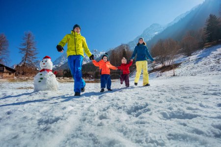 Foto de Padres e hijos corriendo tomados de la mano con sus hijos pequeños en el campo nevado sobre picos de montaña - Imagen libre de derechos
