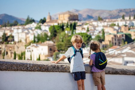 Young travelers stand with backpack on shoulders observe skyline of Ronda during their summer sightseeing trip in Spain