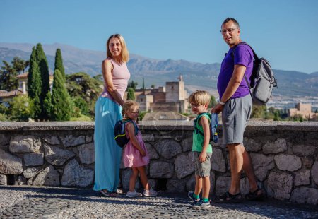 Téléchargez les photos : Les voyageurs avec des enfants debout sur le belvédère profitent de la vue sur le magnifique palais antique de l'Alhambra lors de leur visite estivale à Grenade, Espagne - en image libre de droit