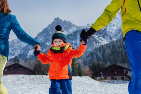Foto de Niño pequeño y feliz llevar sombrero de invierno y abrigo con los padres de las manos corriendo en los Alpes franceses - Imagen libre de derechos