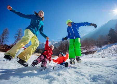 Foto de Dinámica de tiro de madre feliz con tres niños divertirse y saltar en el bosque de montaña nevado en el día soleado - Imagen libre de derechos