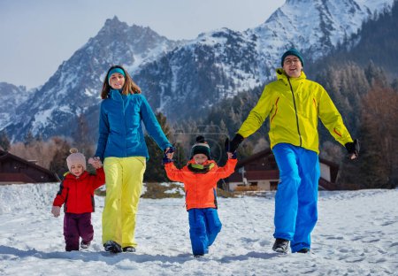 Foto de Riendo familia con niños corriendo juntos tomados de la mano en la nieve blanca en el bosque de montaña con traje de invierno - Imagen libre de derechos