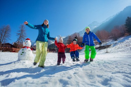 Téléchargez les photos : Mère avec trois enfants bonding sauter sur un champ de montagne enneigé dans les Alpes françaises profiter des vacances d'hiver à Noël - en image libre de droit