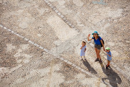 Foto de Turistas madre con niños hacer turismo en España Peniscola casco antiguo, caminar por la calle pavimentada, mirar hacia arriba y saludar, vista desde arriba - Imagen libre de derechos