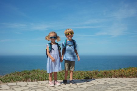 Téléchargez les photos : Heureux frères et sœurs avec des tenues marines d'été se tiennent à fond océanique par une journée chaude au Portugal, en Europe - en image libre de droit