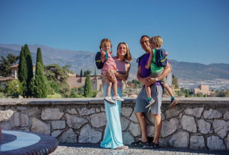 Foto de Familia feliz durante su viaje de verano de pie en el mirador mirando a la cámara con Alhambra antiguo palacio de fondo, Granada, España - Imagen libre de derechos