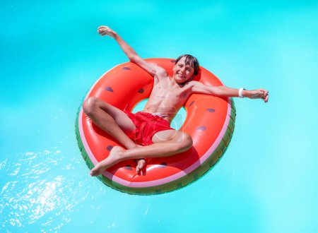 Foto de Un adolescente toma el sol, tumbado en una vibrante piscina inspirada en la sandía flotando, radiante alegría y la esencia de la diversión veraniega - Imagen libre de derechos