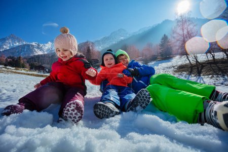 Foto de Felices hermanos ruedan en la nieve sobre soleadas montañas nevadas picos disfrutar de vacaciones de invierno resort - Imagen libre de derechos