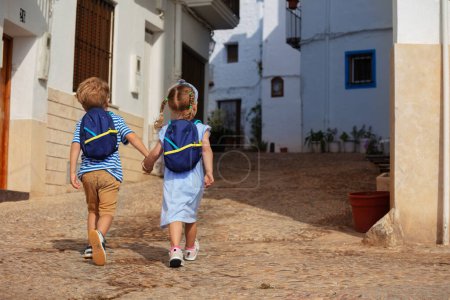 Foto de Jóvenes exploradores chico, chica cogida de la mano caminan por las viejas calles de Peniscola, disfrutando del verano mediterráneo y la arquitectura de España, vista desde la parte posterior - Imagen libre de derechos