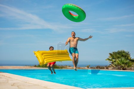 Téléchargez les photos : Un enfant en duo et son père profite d'une journée de piscine vibrante, criant bondissant avec des inflatables sous le ciel lumineux - en image libre de droit