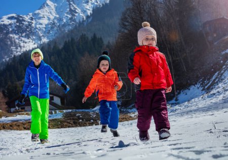 Foto de Acción de tiro de hermanos felices corren en pueblo de montaña en la nieve blanca y picos llamativos en el fondo - Imagen libre de derechos