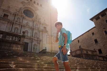 Photo for Handsome teenage boy with backpack climb up the famous stairs of Cathedral of Girona during his vacations in Spain at sunny day - Royalty Free Image