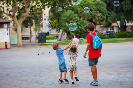 Foto de Los niños felices se divierten y tratan de atrapar las enormes burbujas de jabón en el día de verano en la plaza de Valencia, España - Imagen libre de derechos
