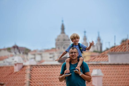 Téléchargez les photos : Enfant excité sur les épaules des pères observant Lisbonne du point de vue de la ville, les toits et l'église en arrière-plan - en image libre de droit