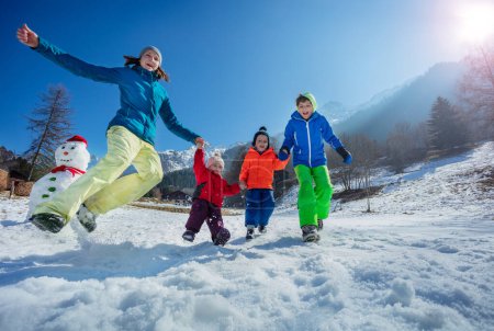 Foto de Acción tiro de feliz familia madre con tres niños divertirse y saltar en el bosque de montaña nevado en el día soleado - Imagen libre de derechos
