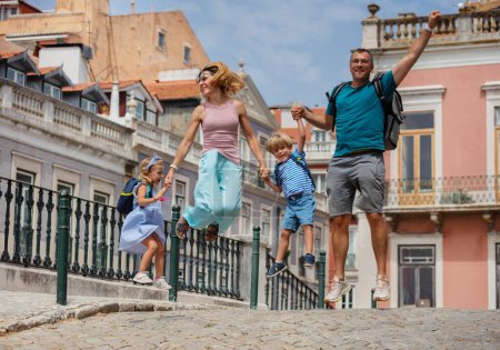 Foto de Jóvenes viajes en familia con niños saltan felices, la arquitectura de Lisboa en el fondo - Imagen libre de derechos