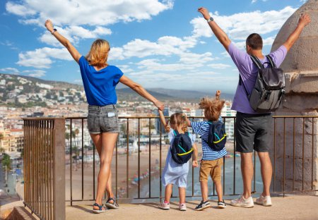 Foto de Familia con niños levantan las manos emocionados en su visita a España disfrutar de la costa y la playa vista desde el punto de observación del castillo de Peniscola en el soleado día de verano - Imagen libre de derechos