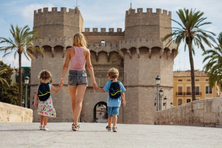 Téléchargez les photos : Mère avec deux enfants marchent sous le soleil de Valence devant les célèbres Torres de Serranos pendant leurs vacances d'été en Espagne - en image libre de droit