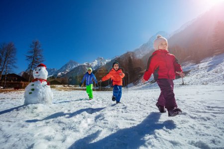 Foto de Grupo de niños corriendo en el soleado campo de nieve en las montañas francesas disfrutando de las vacaciones de invierno - Imagen libre de derechos