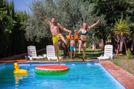 Foto de Familia de felices nadadores tomados de la mano, gritan, capturados en movimiento de salto en la hermosa piscina del resort en sus vacaciones de verano - Imagen libre de derechos