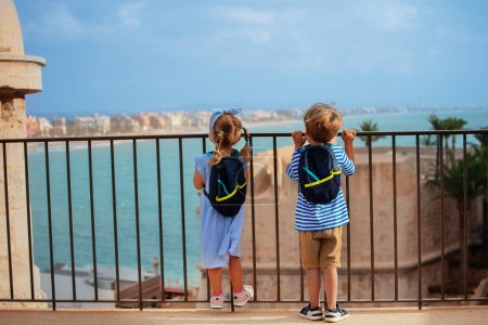 Foto de Dos lindos turistas, chico, chica visitando España observan la vista de la costa, se paran en el punto de observación del castillo de Peniscola en el soleado día de verano - Imagen libre de derechos