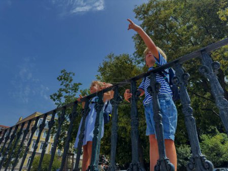 Téléchargez les photos : Jeunes, garçon et fille en tenue d'été au belvédère de Lisbonne pointant du doigt, arbres verts sur le fond, vue d'en bas - en image libre de droit