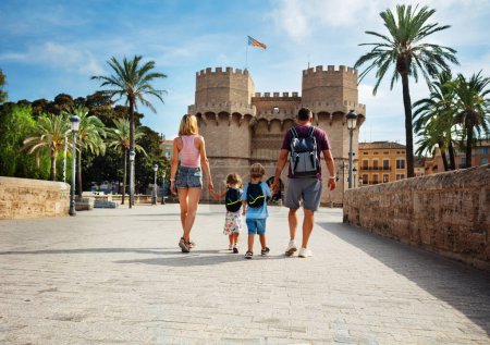 Téléchargez les photos : Les parents avec deux enfants marchent sous le soleil de Valence devant les célèbres Torres de Serranos pendant leurs vacances d'été en Espagne, vue de derrière - en image libre de droit
