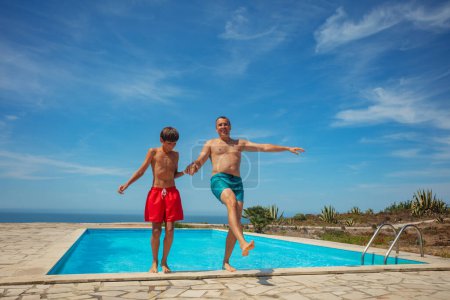 Foto de Con los brazos levantados, un hombre y un niño expresan su emoción mientras saltan hacia atrás en el abrazo fresco de una piscina del patio trasero - Imagen libre de derechos