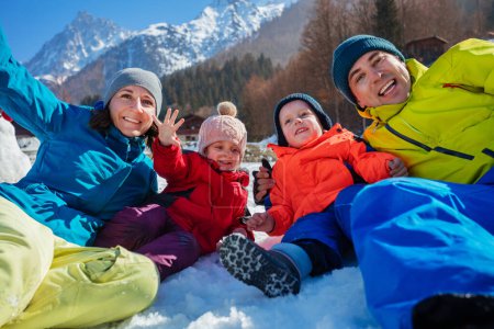 Foto de Familia feliz con niños pequeños en vacaciones de invierno abrazándose en la nieve sobre las montañas agitadas saludando mirando a la cámara - Imagen libre de derechos