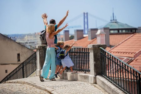 Foto de Feliz familia joven en vacaciones en Europa levantar las manos mirando el puente de Lisboa desde el punto de observación en el día soleado - Imagen libre de derechos