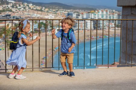 Téléchargez les photos : Deux enfants heureux visitant l'Espagne profitent d'une vue sur le littoral et dansent sur le point d'observation du château de Peniscola le jour ensoleillé de l'été - en image libre de droit