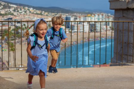 Foto de Dos lindos turistas, chico, chica visitando España les encanta la vista de la costa, saltar y bailar en el punto de observación del castillo Peniscola en el soleado día de verano - Imagen libre de derechos