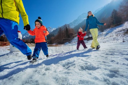 Foto de Hermosa familia con niños pequeños corriendo en el campo nevado sobre picos de montaña soleados, disfrutar de vacaciones de invierno - Imagen libre de derechos