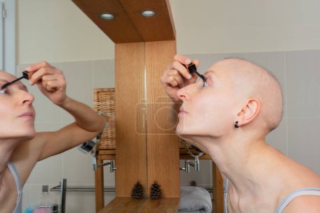 Foto de Una escena de baño donde una persona femenina se aplica cuidadosamente maquillaje a sus pestañas usando una varita de rímel, se mantiene fuerte con cáncer - Imagen libre de derechos