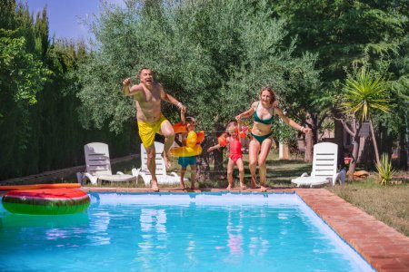 Photo for Joyful parents with their children are about to plunge together into a clear blue pool, surrounded by summer lush greenery of backyard - Royalty Free Image