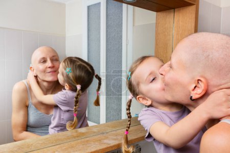 Foto de Una mujer calva recibe alegremente un beso en la mejilla de una joven con el pelo trenzado mientras está sentada en un baño - Imagen libre de derechos