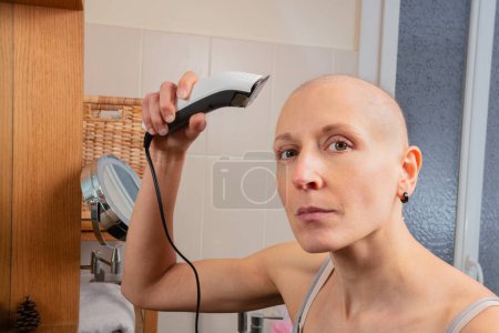 Photo for Woman with a bald head skillfully gives herself a trim using a hair shaving appliance in front of the mirror - Royalty Free Image