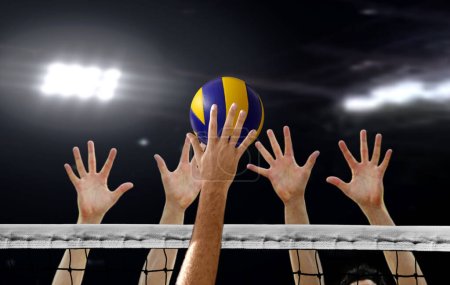 Photo for Close up of Volleyball spiking and hand blocking over the net under bright spotlights - Royalty Free Image