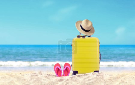 Foto de Yellow luggage with hat and red flip-flop on sandy beach under blue sky background. - Imagen libre de derechos