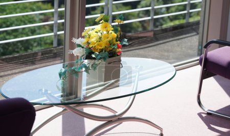 Florale Dekoration auf einem Glastisch in einem Raum mit Licht, das an einem sonnigen Tag vom Fenster aus beleuchtet wird                               
