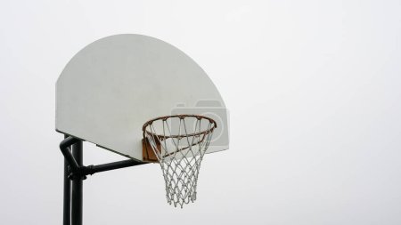 A single basketball hoop stands tall with its white backboard and orange rim, poised against a clear, pale sky, awaiting players to commence a game.