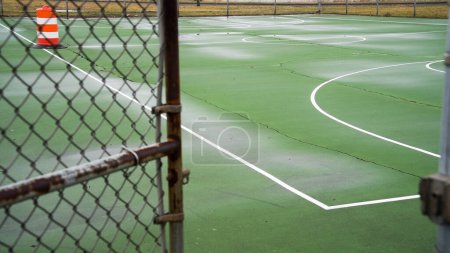 Empty outdoor green basketball court with visible cracks and white linesThe court awaits players on what appears to be an overcast day, with no equipment or people in sight.