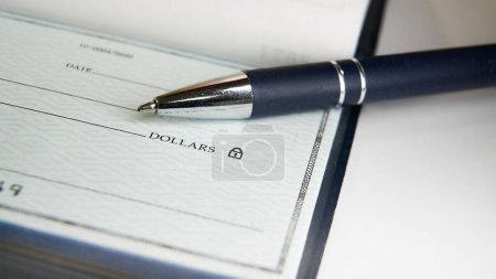 A blue pen is poised on a blank check with its tip resting near the payment amount line, ready for someone to fill out the necessary details for a financial transaction.